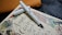 A white fountain pen rests diagonally on a book titled 'Angela Carter's Book of Fairy Tales.' The book features whimsical illustrations of mythical creatures and intricate designs. The background includes a subtle texture with a leather-like object in brown color.