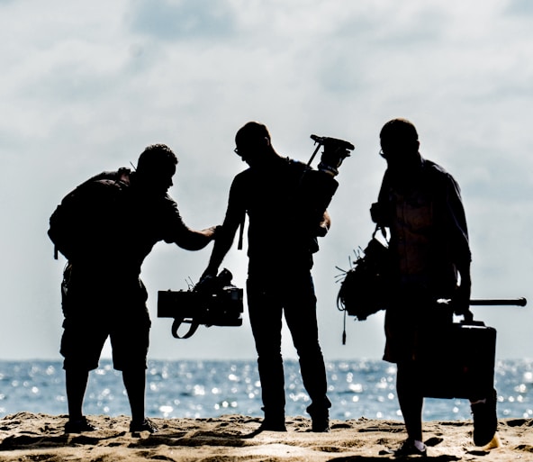 silhouette of men holding camera standing on sand near body of water during daytime