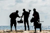 silhouette of men holding camera standing on sand near body of water during daytime