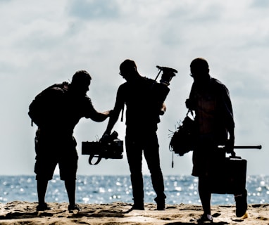 silhouette of men holding camera standing on sand near body of water during daytime