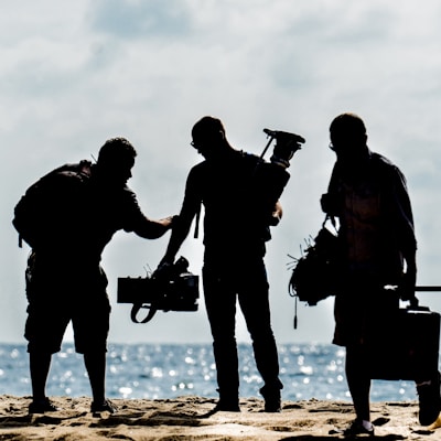 silhouette of men holding camera standing on sand near body of water during daytime