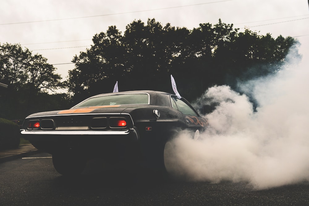 black coupe with wheels covered in smoke