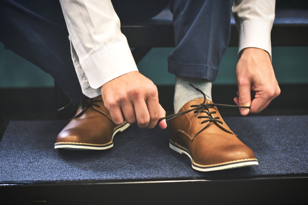 person tying brown leather shoes