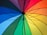 A colorful umbrella with sections of various colors arranged in a radial pattern. The colors include red, orange, yellow, green, blue, and purple, creating a vibrant and eye-catching design.