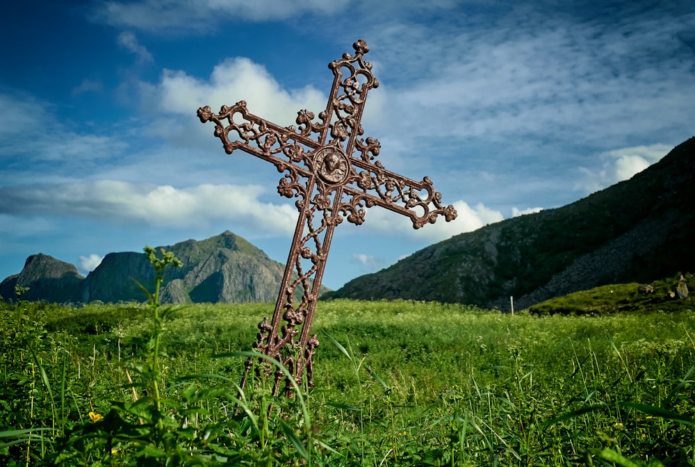 leaning brown metal cross on green grass field near mountains at daytime