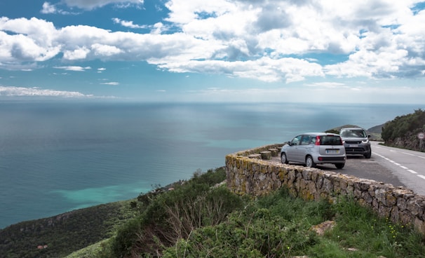 A car parked safely at a lookout point overlooking the ocean and mountains.
