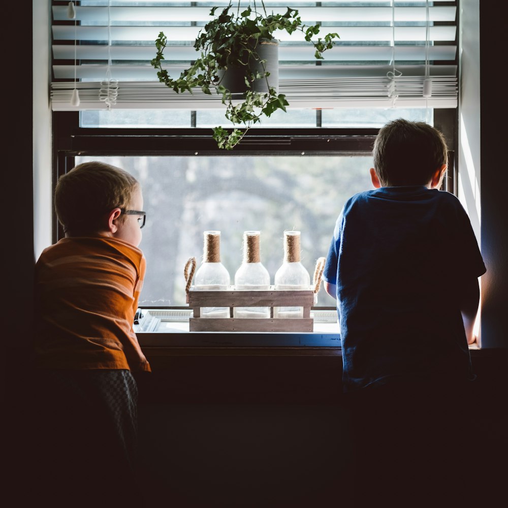 dois meninos em pé na frente da janela