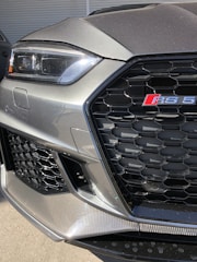 Close-up of a sleek Audi RS3 grille with sporty LED headlights glowing.
