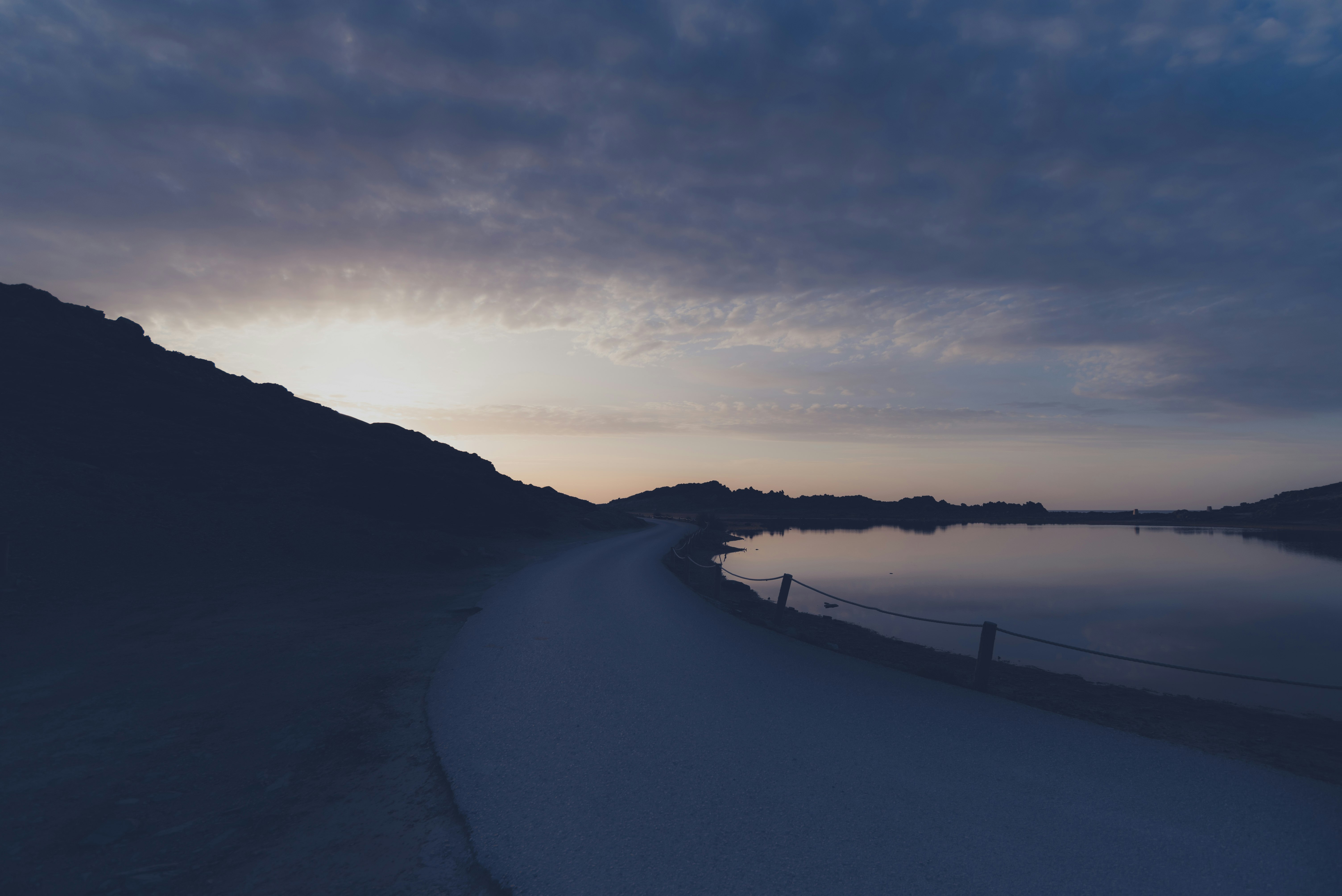 concrete road near body of water during sunrise