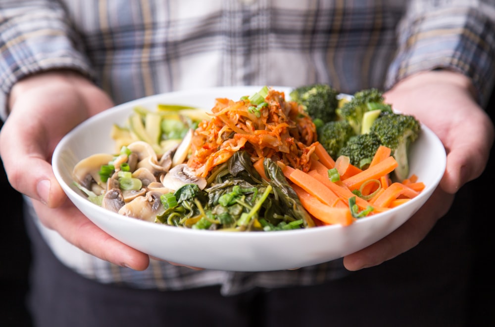 person holding plate with vegetables