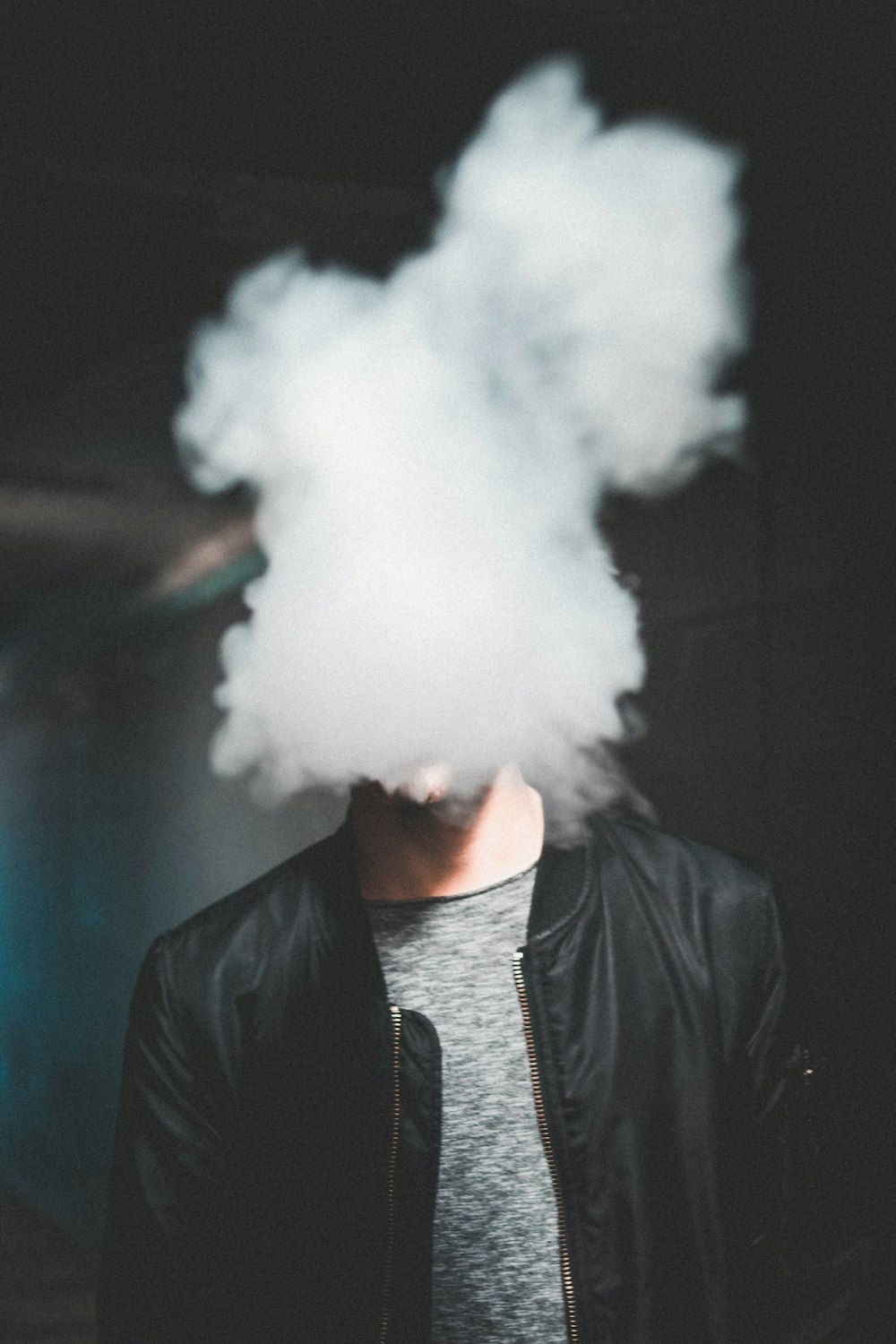 Mann trägt schwarze Lederjacke mit Reißverschluss, während er Rauch bläst