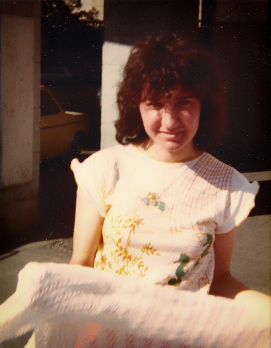 A casually dressed person wearing a neutral-tone plain t-shirt, standing outdoors with soft sunlight highlighting the fabric texture.