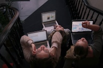 three person using laptops while sitting on ladder