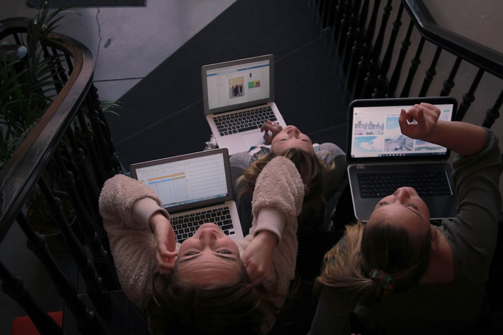 three person using laptops while sitting on ladder