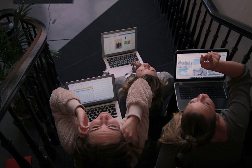 três pessoas usando laptops enquanto sentadas na escada