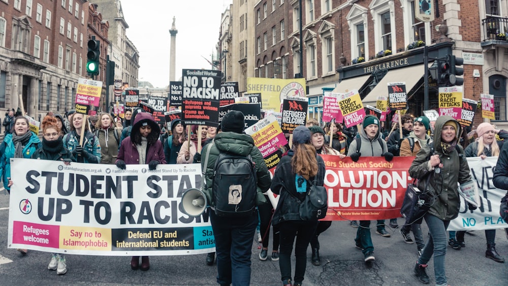 people walking on street holding banner in between building during daytime