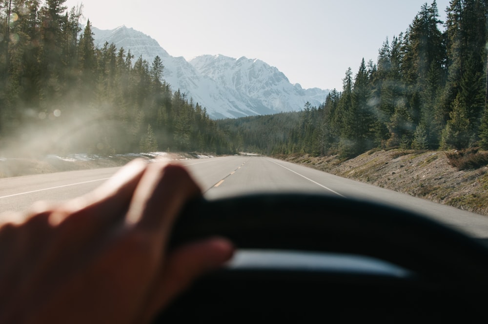 a person driving a car on a road with mountains in the background