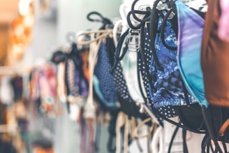 A collection of colorful bikinis on display, hanging in a row. The designs include various patterns such as polka dots and abstract prints. The image has a soft focus on the left side, drawing attention to the vibrant swimwear.