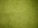 A close-up view of a green grassy surface, densely covered with neatly trimmed blades of grass. The texture is uniform, indicating well-maintained lawn or artificial turf.