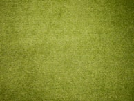 A close-up view of a green grassy surface, densely covered with neatly trimmed blades of grass. The texture is uniform, indicating well-maintained lawn or artificial turf.
