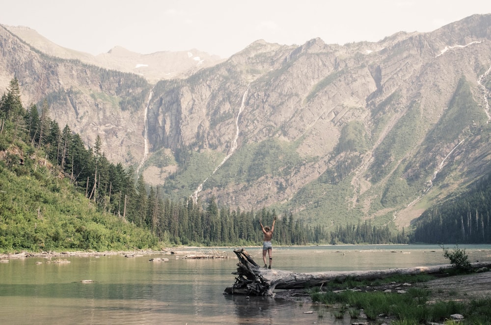 person standing on dead tree facing body of water