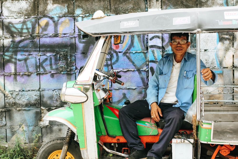 man sitting on auto rickshaw near graffiti wall during daytime