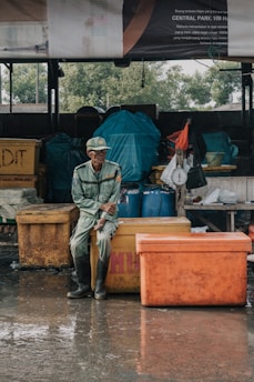 man sitting on yellow fish box during day