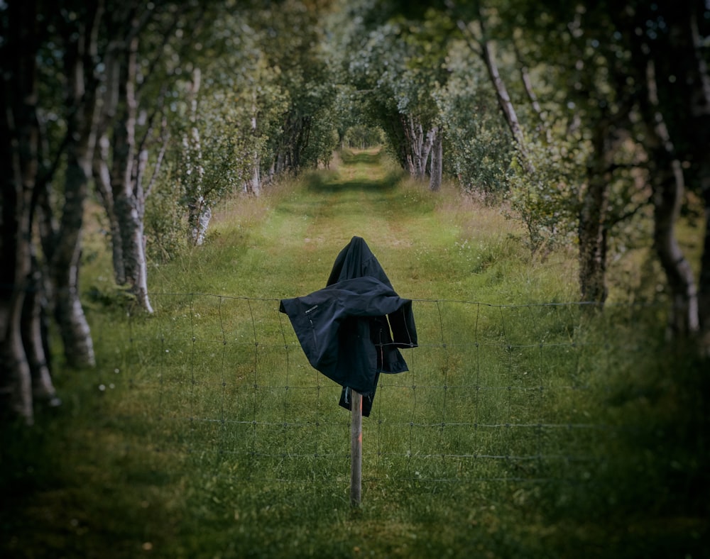 cappotto nero sulla recinzione vicino agli alberi