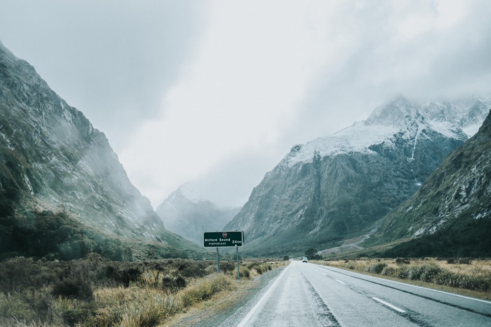 gray concrete road between mountains and brown grasses at daytime