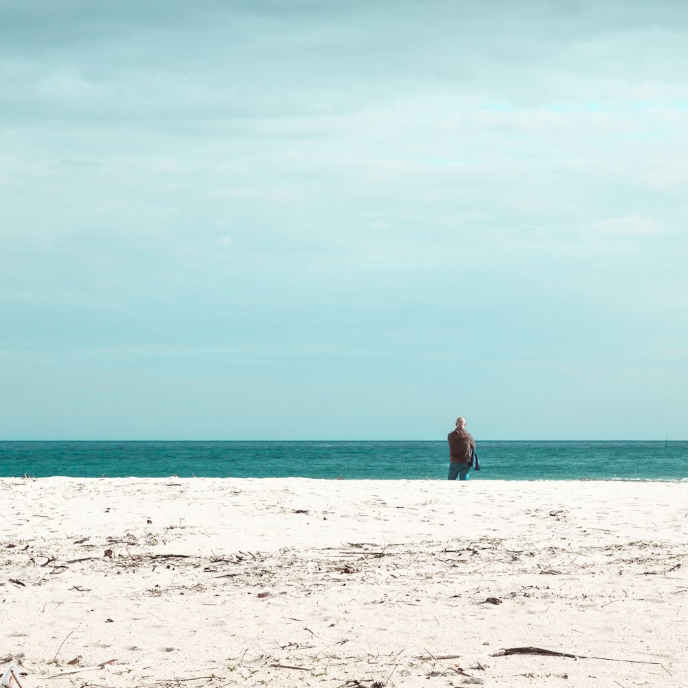 man standing on white sand beach during daytime
