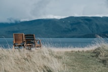 two brown wooden armchairs in front of body of water