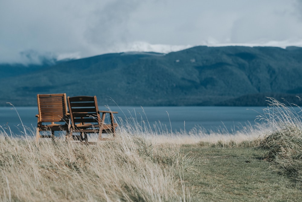 two brown wooden armchairs in front of body of water