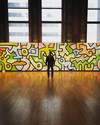 man wearing black jacket and pants facing multicolored graffiti