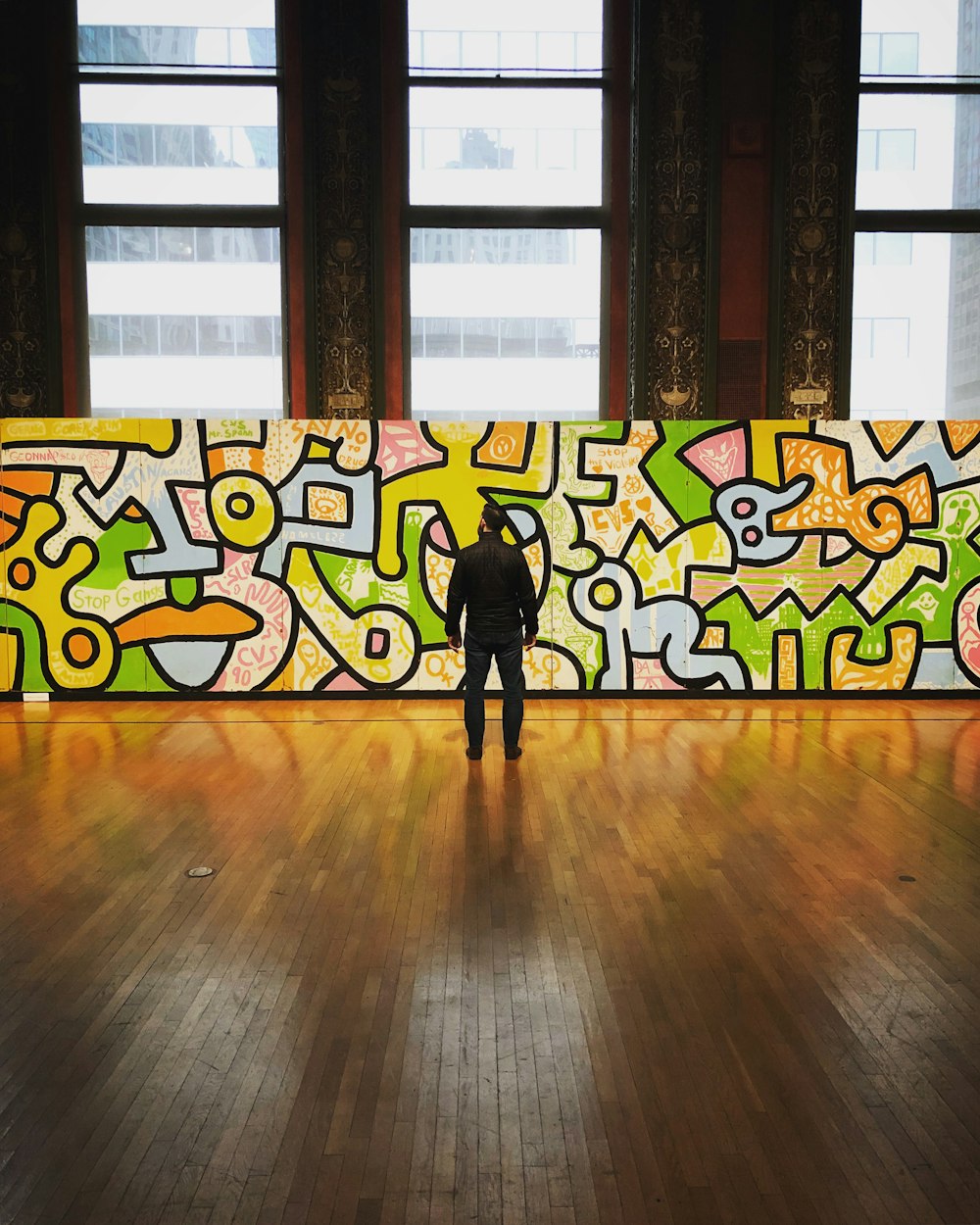 man wearing black jacket and pants facing multicolored graffiti