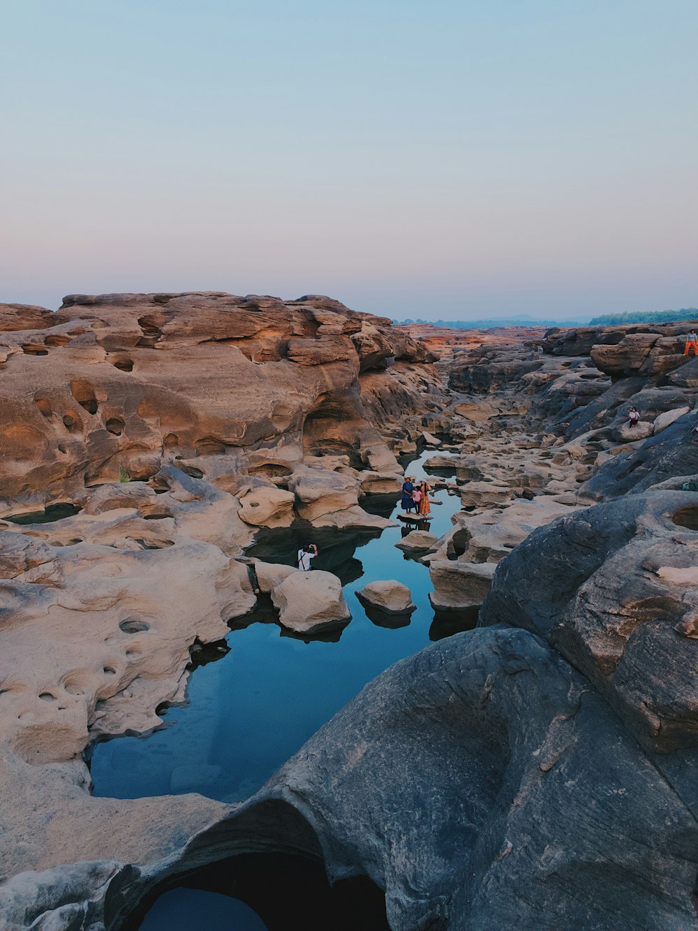 two persons sitting on rock at the middle of body of water