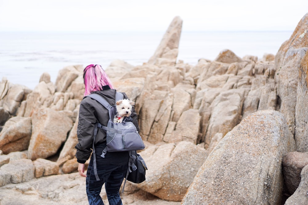 woman walking near rock formations in front of sea during daytime