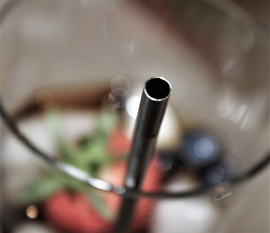 Close-up of shiny metal straws arranged neatly on a wooden table with green leaves around.