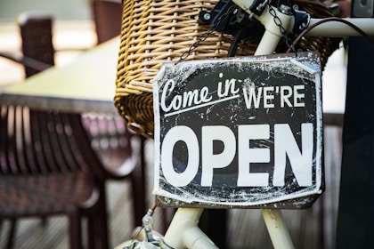 black and white come in we're open signage pinned on white bicycle with brown wicker basket at daytime