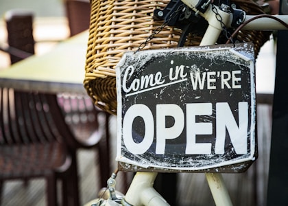 black and white come in we're open signage pinned on white bicycle with brown wicker basket at daytime