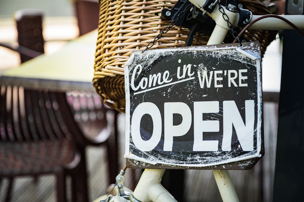 black and white come in we're open signage pinned on white bicycle with brown wicker basket at daytime