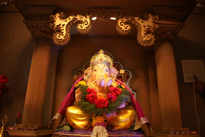 A serene Ganpati idol adorned with saffron and gold accents, placed on a traditional wooden altar.
