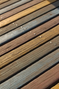 Wooden planks arranged side by side with distinct grain patterns and varying colors, including shades of brown, yellow, and blue. Small metallic screws are visible on the surface.