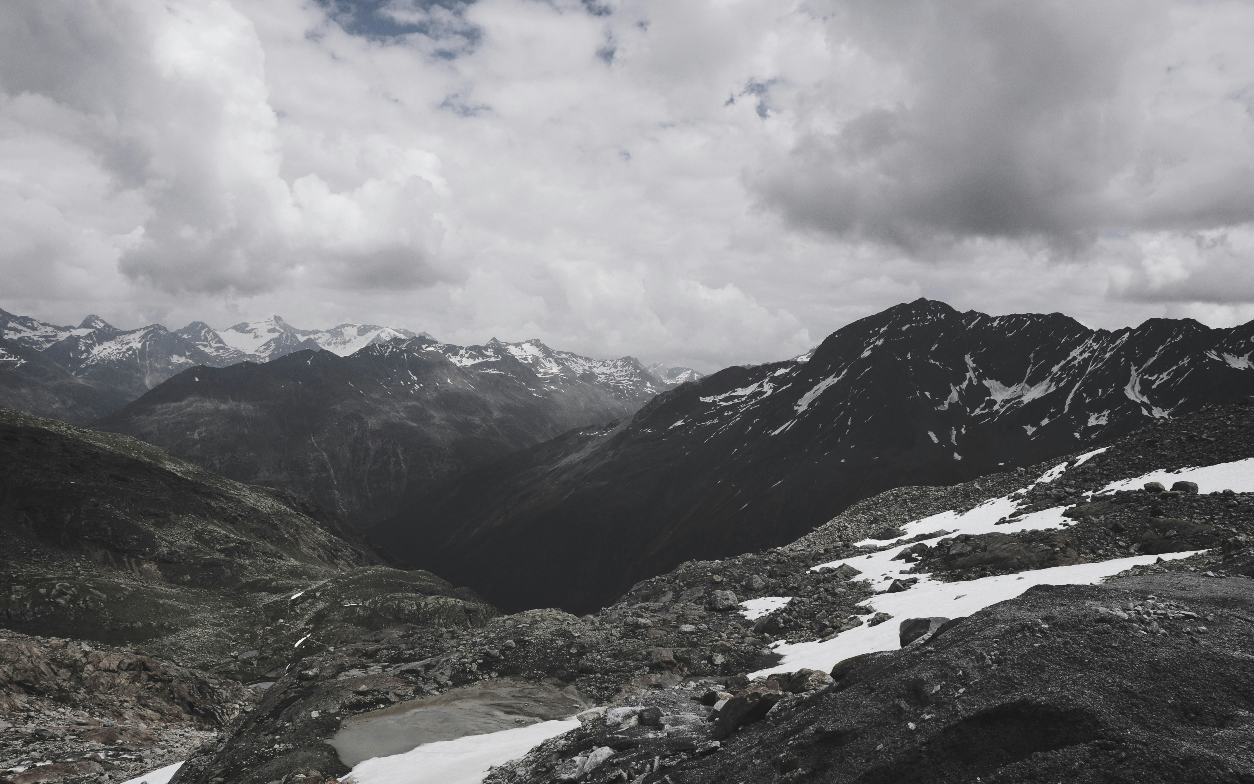 Mountain terrain at high altitude, snow-capped peaks, dramatic grey sky, rugged landscape