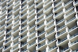 A grid-like pattern of white balconies on a modern high-rise building, featuring clear glass railings and dark window frames.