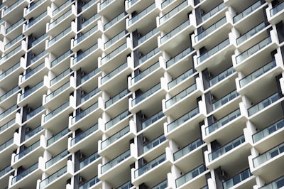 A grid-like pattern of white balconies on a modern high-rise building, featuring clear glass railings and dark window frames.