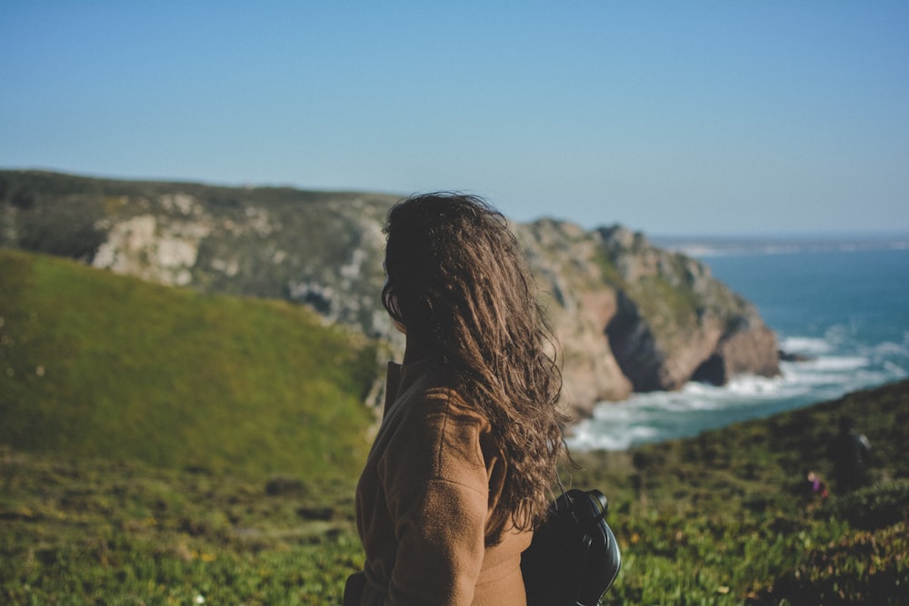 woman looking at cliffs while ocean waves are pounding it during daytime