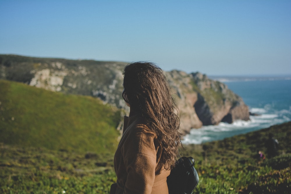 femme regardant les falaises pendant que les vagues de l’océan le martèlent pendant la journée