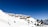 A series of wooden cabins are nestled on a snow-covered hill. The scene is set against a clear, deep blue sky. Small patches of evergreen trees dot the snowy landscape, adding contrast to the whiteness of the snow.