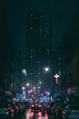 A dark city street with cars lined up, their neon underglow casting colorful reflections on wet pavement.