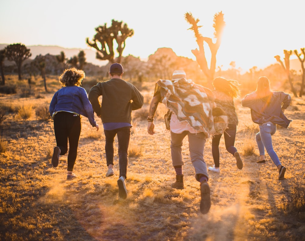 Five people running on a field near some trees